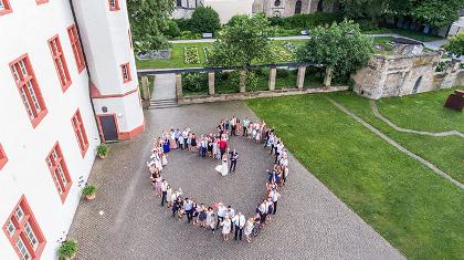 An aerial view of a group of wedding guests forming a heart around a married couple, as taken by a drone